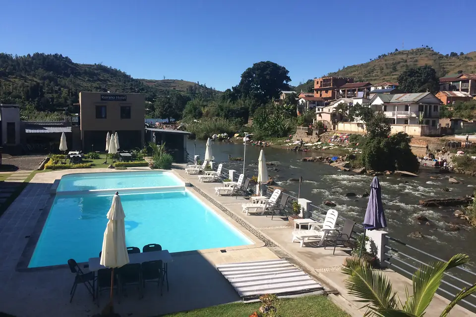 Piscine bordée de transats et de parasols au bord de la rivière, collines en arrière-plan